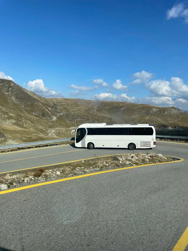 Autocar pe un drum montan cu serpentine, sub cer albastru